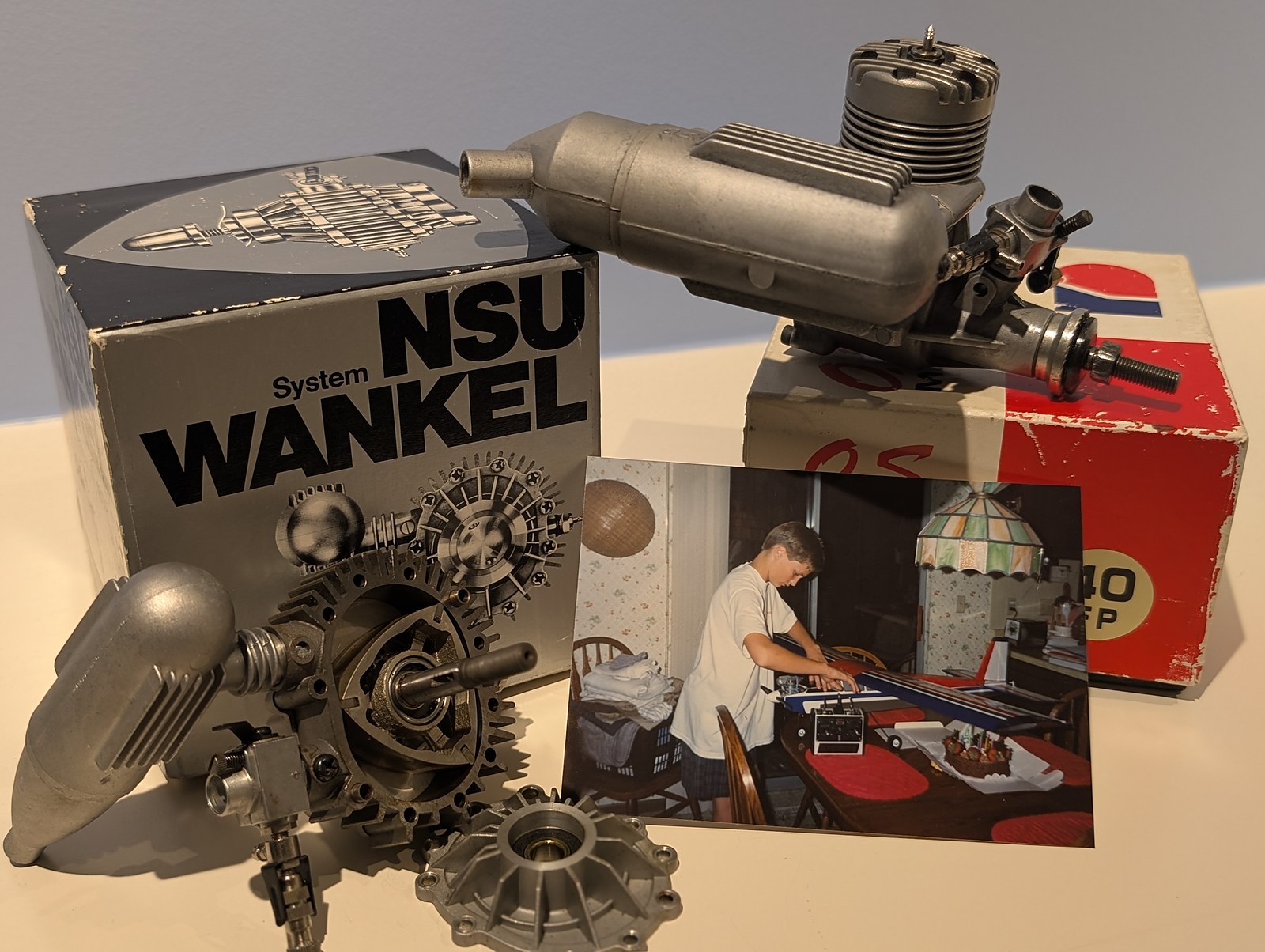 The NSU System Wankel box and disassembled rotary engine beside the OS 40 FP box and engine, with a 1987 snapshot of a boy building a radio-control plane